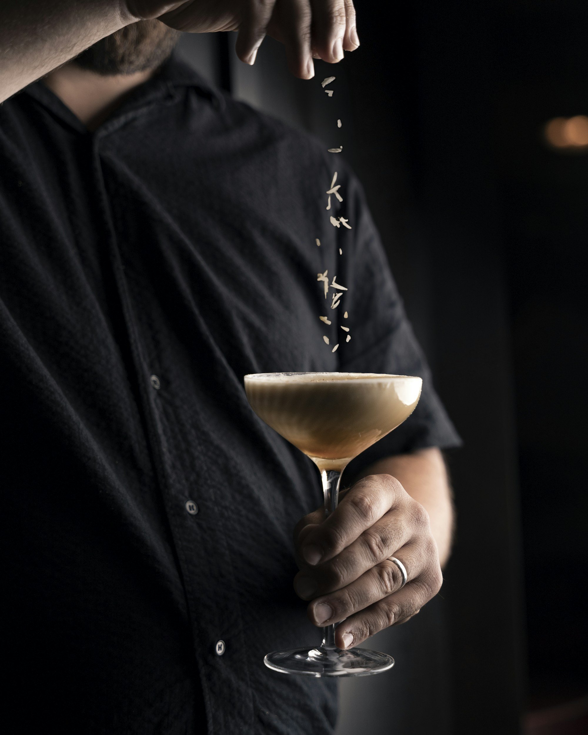Persoon die een cocktailglas vasthoudt terwijl rijst wordt overgegoten in het glas, in een donkere setting.