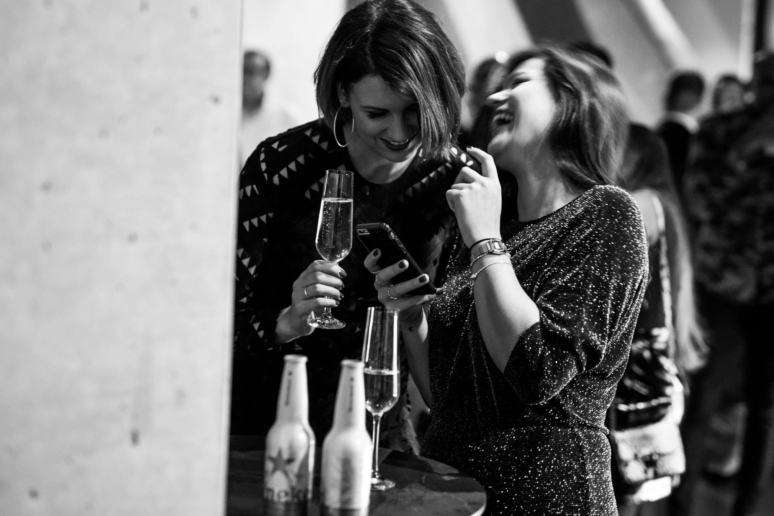 Twee vrouwen lachen en kijken naar een telefoon terwijl ze champagne drinken op een feestje.