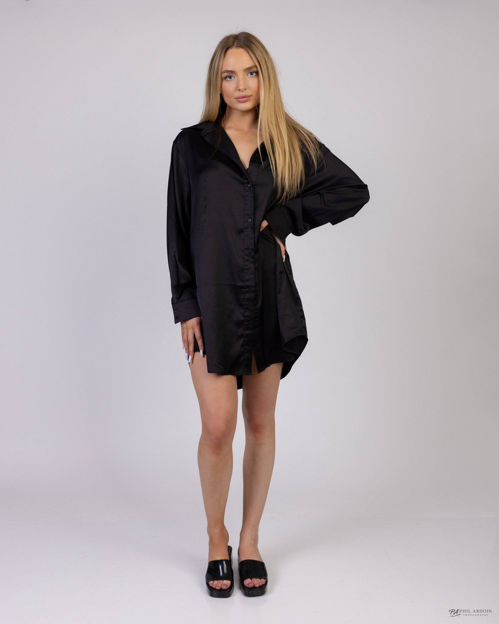 Maddie Jordan in a black shirt dress and heels against a studio backdrop.