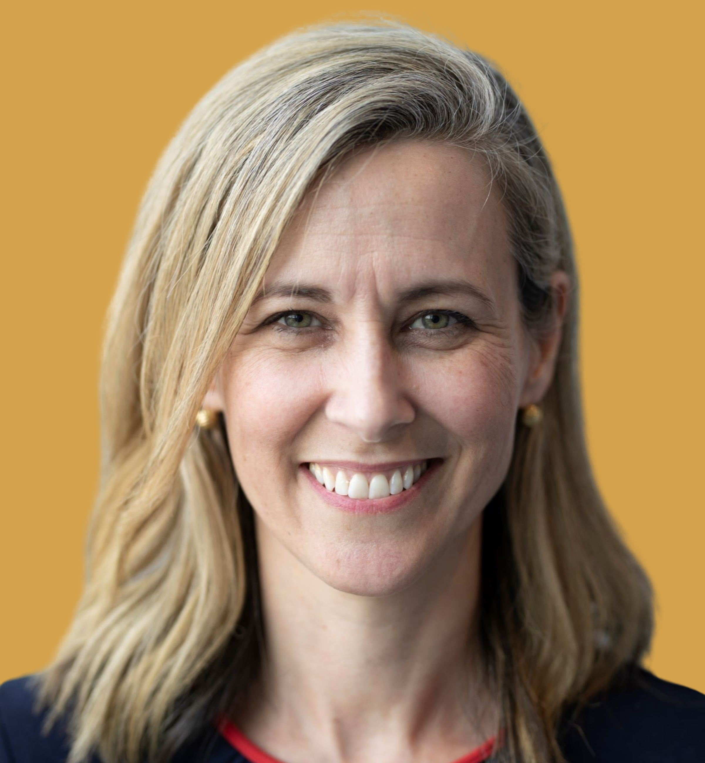 Close-up of a smiling woman with light blonde hair, green eyes, and earrings, against a yellow background.