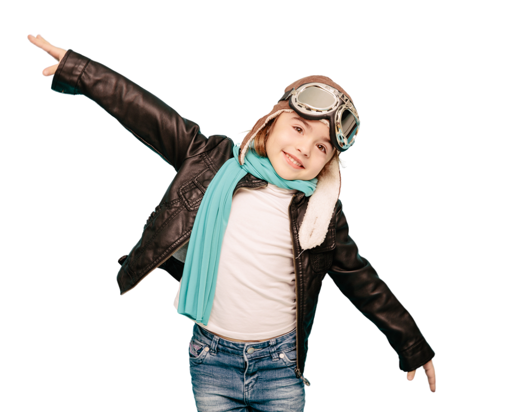 A young girl dressed in a leather jacket, goggles on her forehead, a light blue scarf, and jeans, smiling with arms outstretched.
