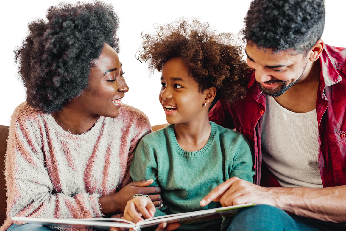 A family of three, a woman, a man, and a young girl, sitting close together, smiling, and looking at each other as they read a book.