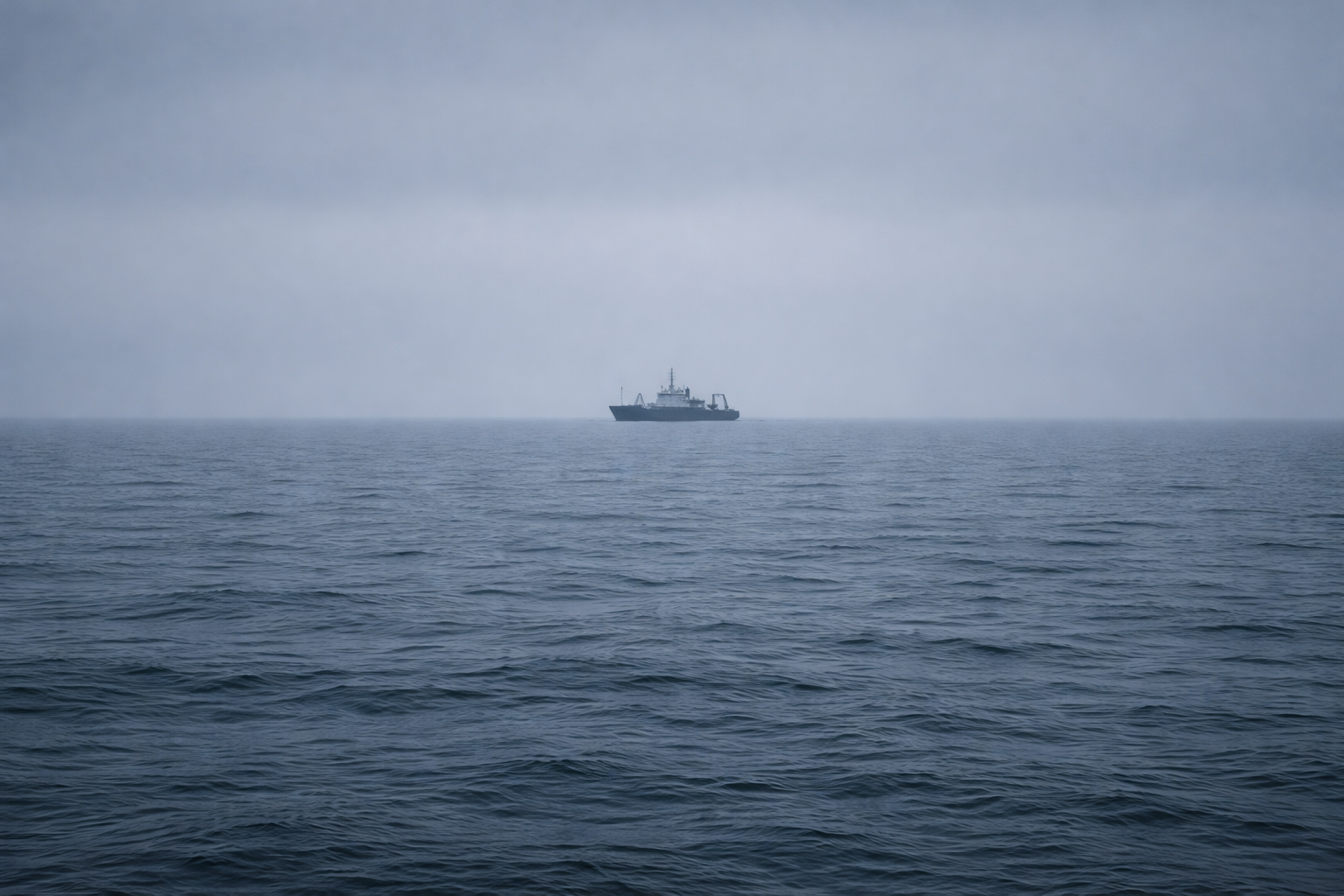 A lone ship on the open ocean under a cloudy sky.
