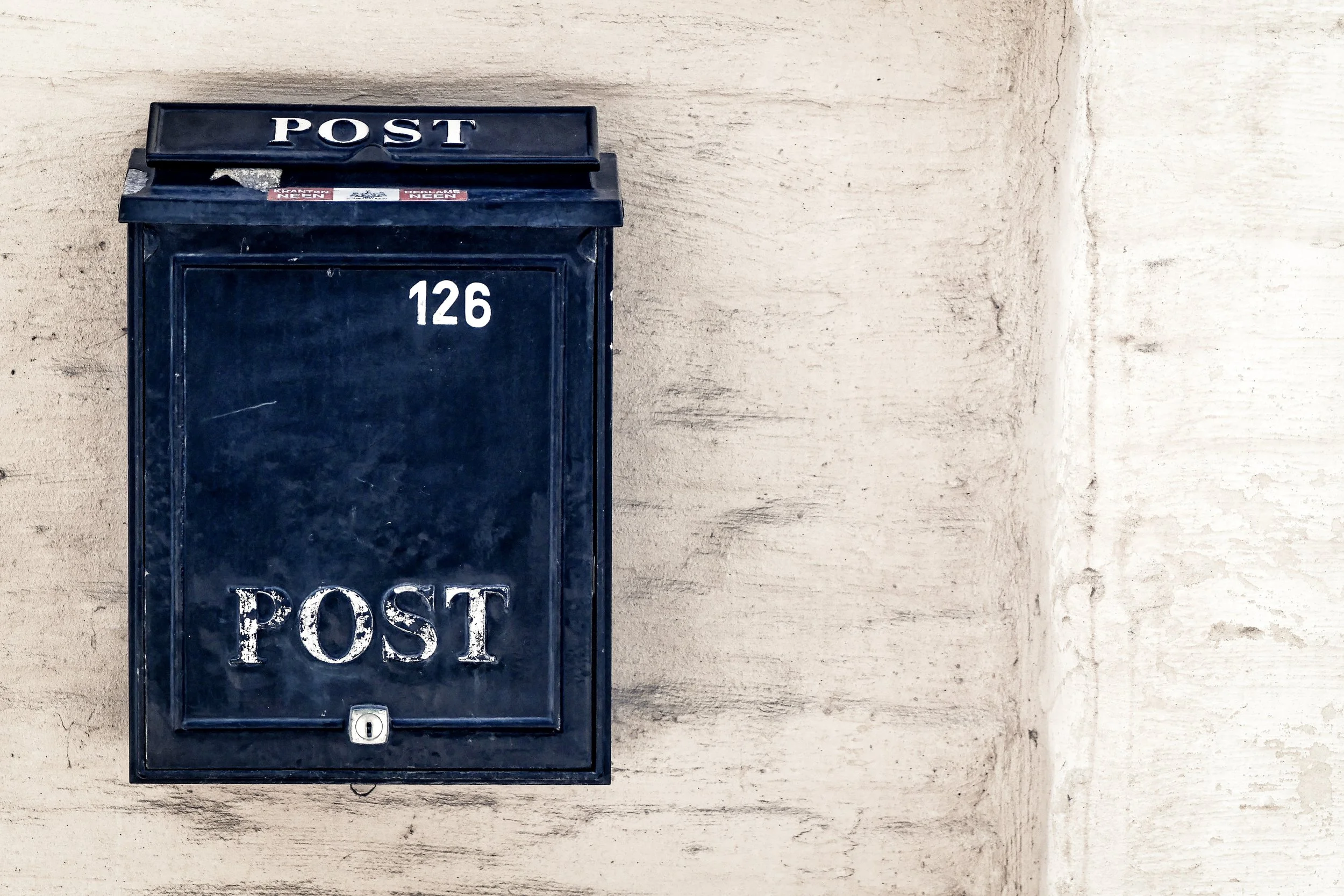A black mailbox with the word 'POST' on the top flap and the number '126' on the front, mounted on a wall.