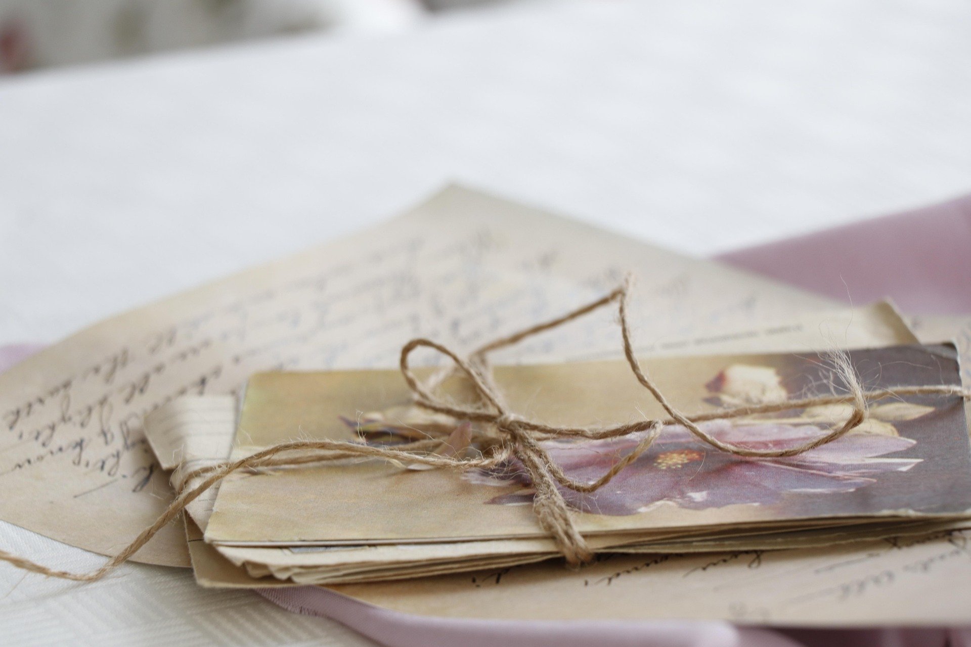 Stacked vintage letters tied with a piece of twine, with handwritten script visible on the top letter, on a light-colored surface.