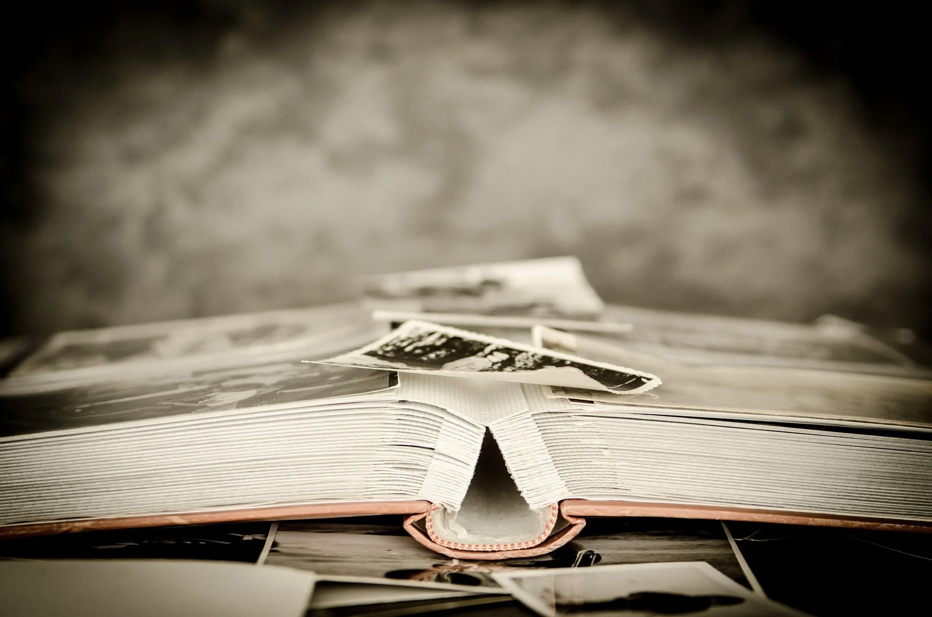 An open photo album with black-and-white photographs and printed images on the pages, placed on a flat surface with a blurred background.