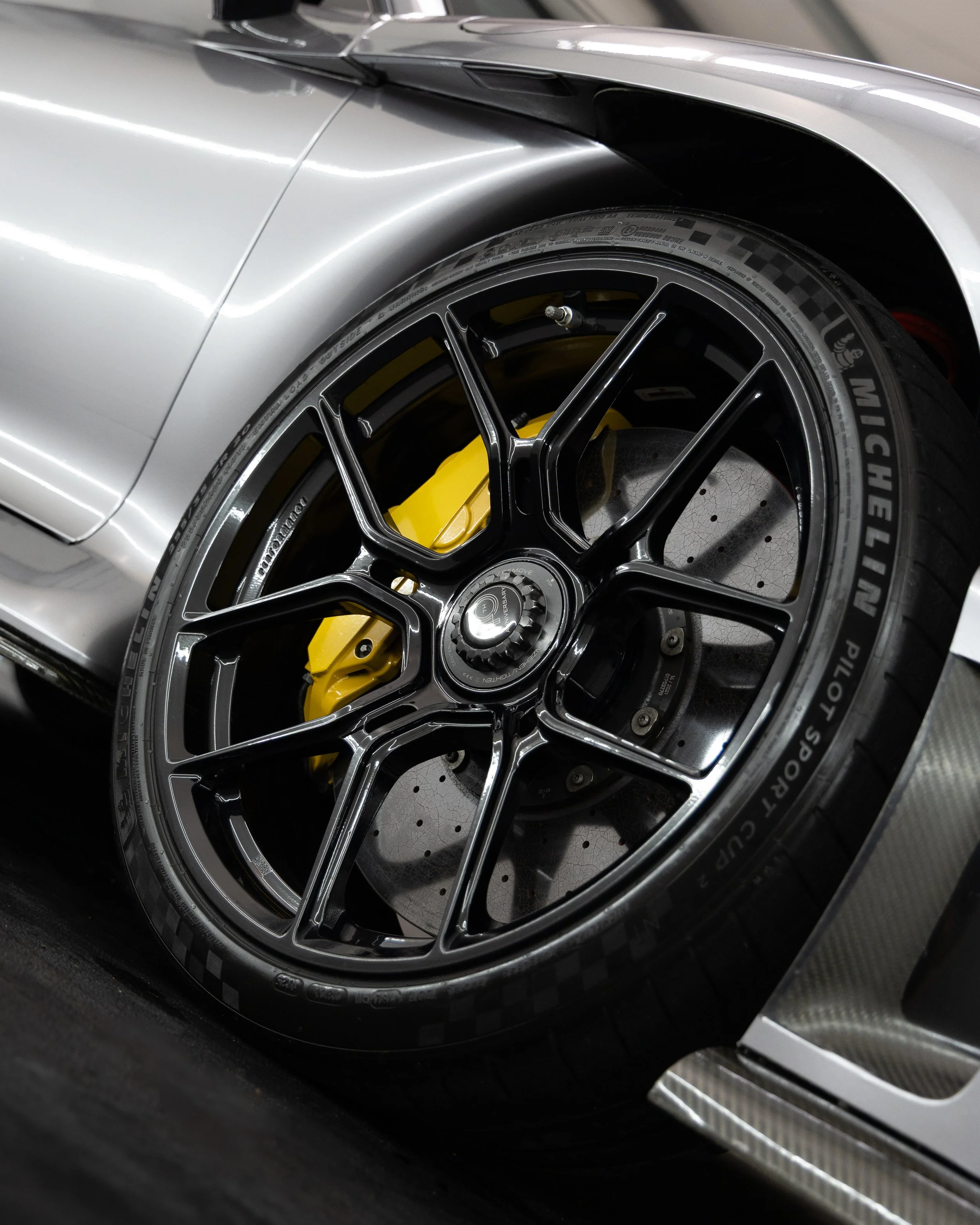 Close-up of a high-performance car wheel with a black multi-spoke rim, yellow brake caliper, and Michelin racing tire.