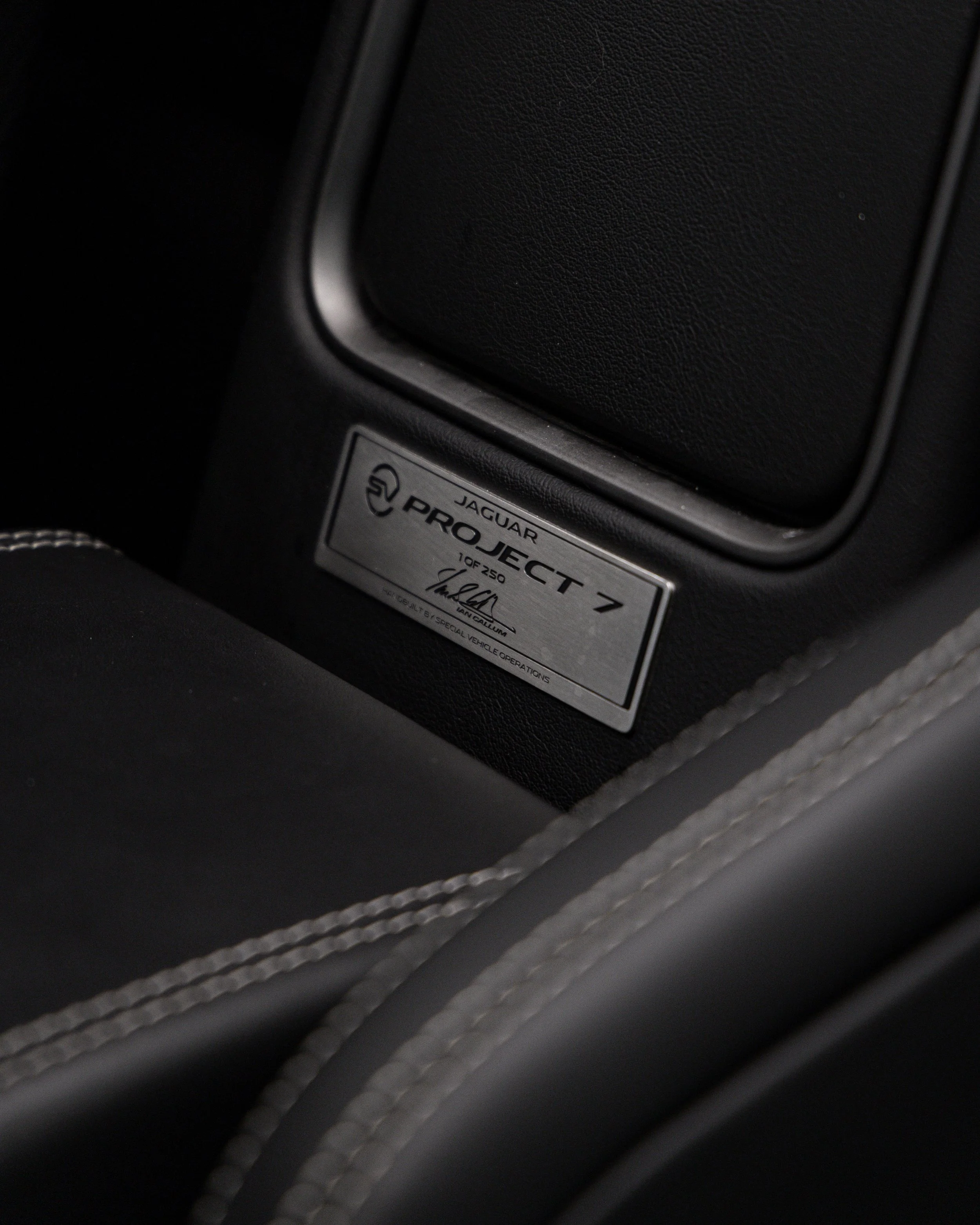 Close-up of a metallic nameplate on a Jaguar car interior that reads 'Jaguar Project 7, 1 of 250' with a signature, mounted on black leather with light-colored stitching.