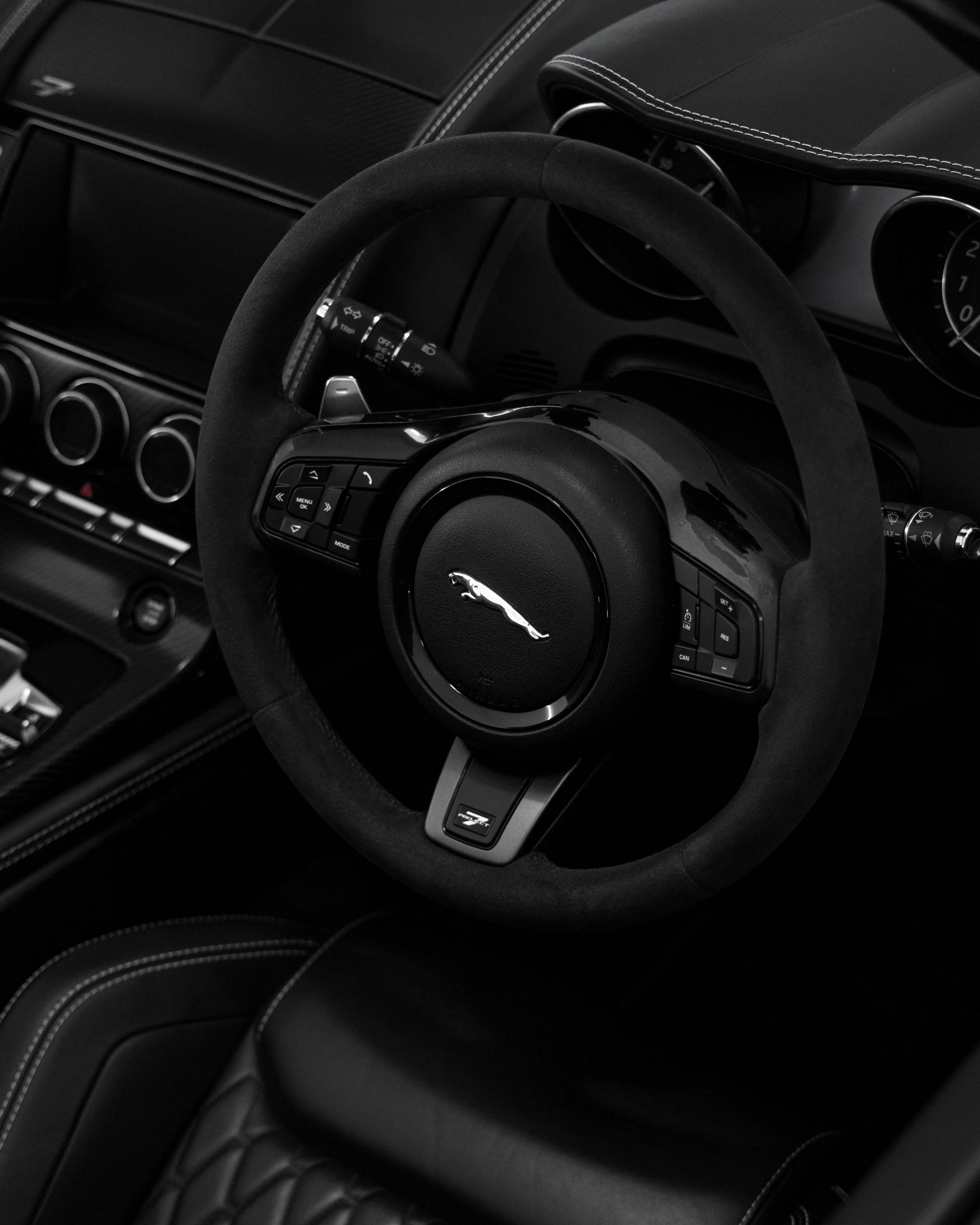 Close-up of a black steering wheel with a Jaguar logo in the center, inside a luxury car interior.