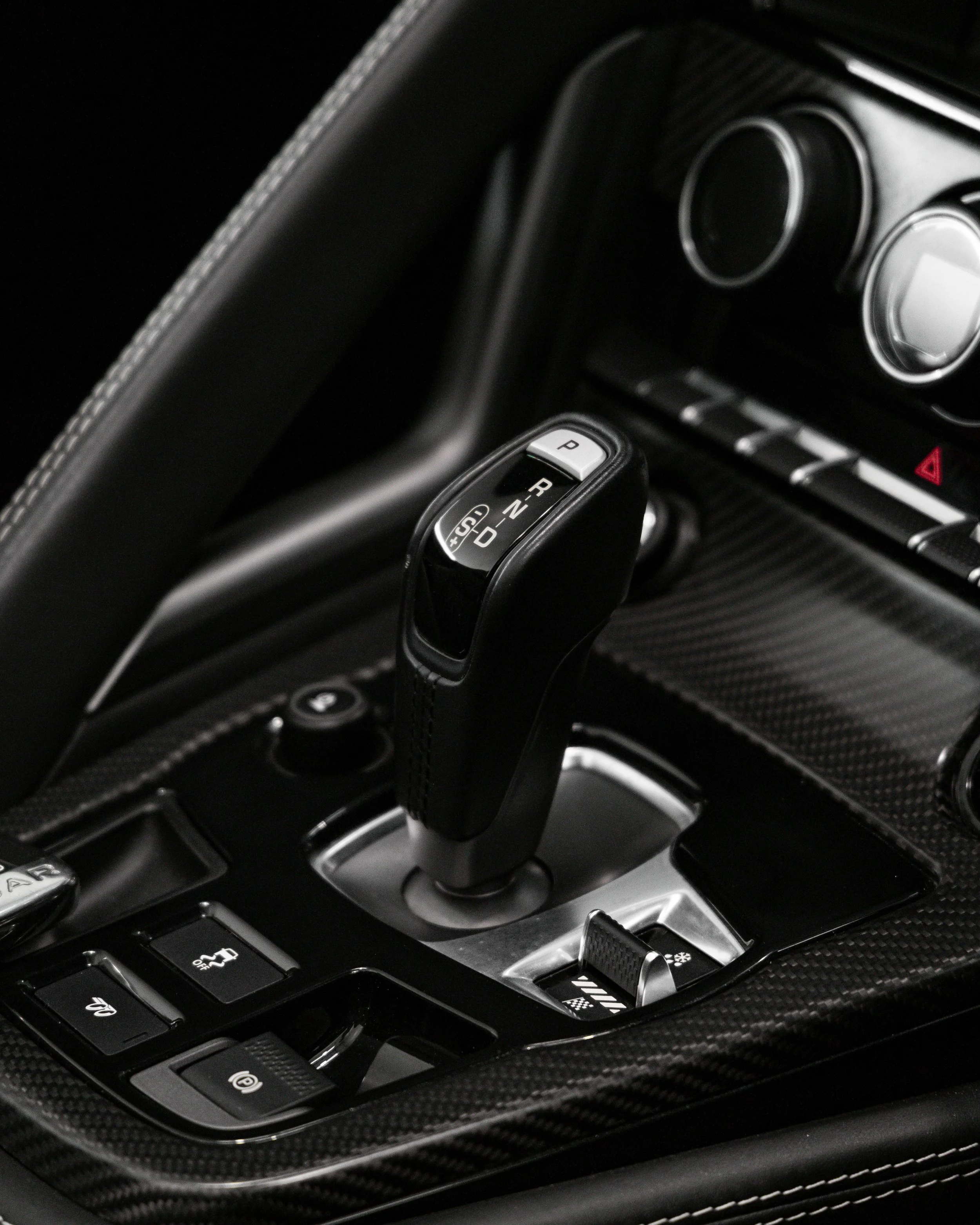 Close-up of a luxury car's gear shifter in a carbon fiber console.