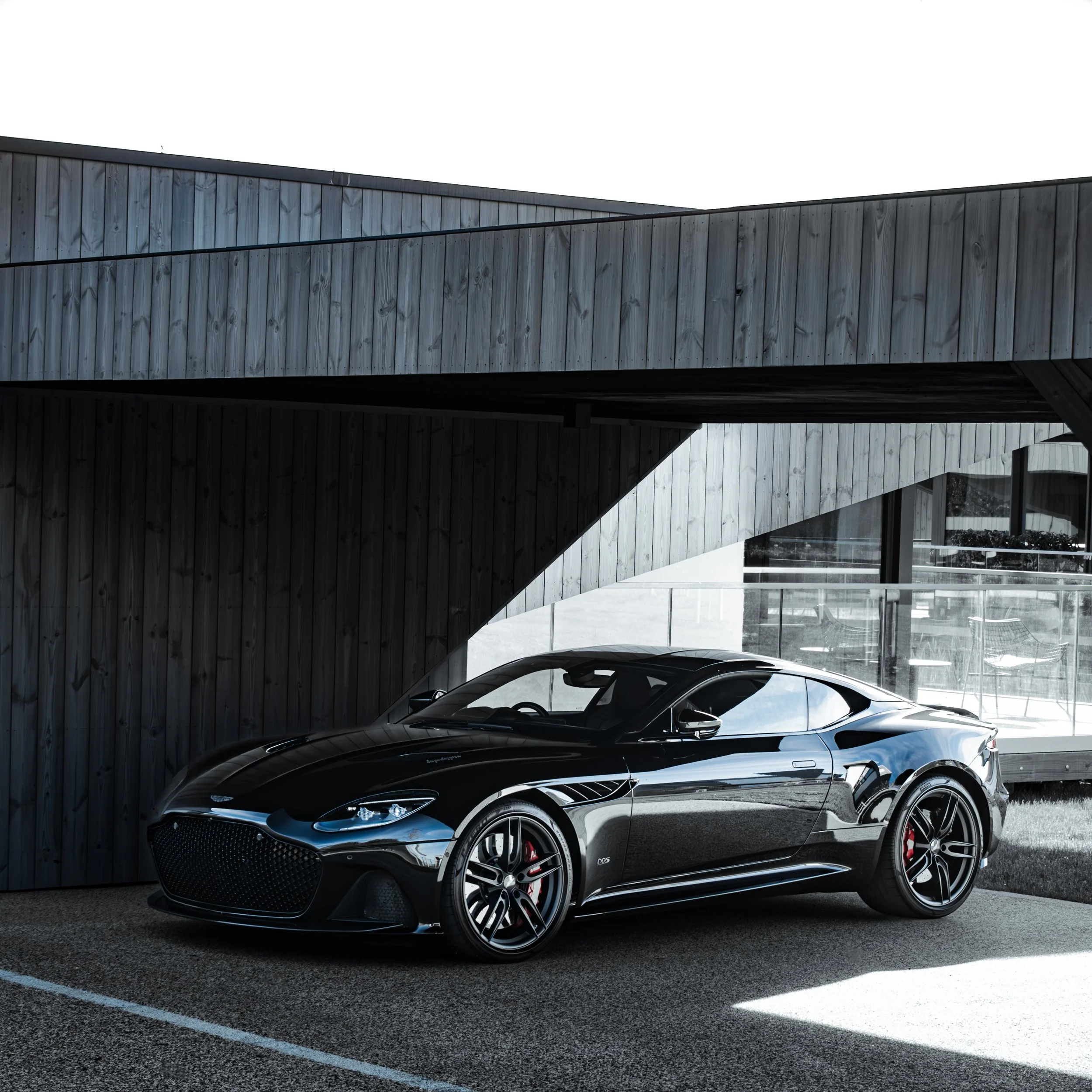 A sleek black sports car parked outside modern building with wooden cladding.