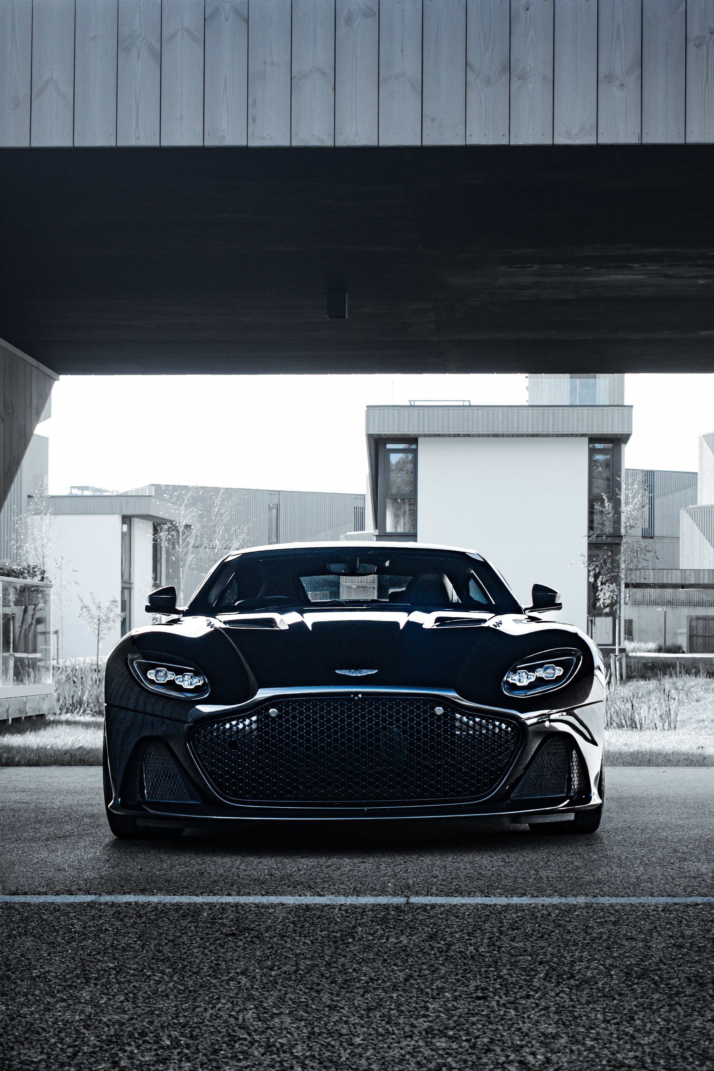 A sleek black sports car parked under a modern building overhang with residential buildings in the background.