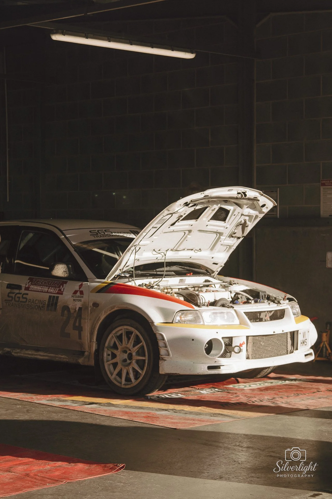 Steve Hill's white evo racing rally car with its hood open, parked inside a garage , at donington.
