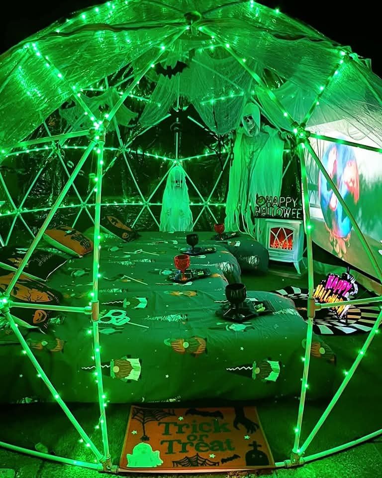 A Halloween-themed indoor setting with green LED lights, ghost decorations, a sign that says "Happy Halloween," and a mat that says "Trick or Treat."
