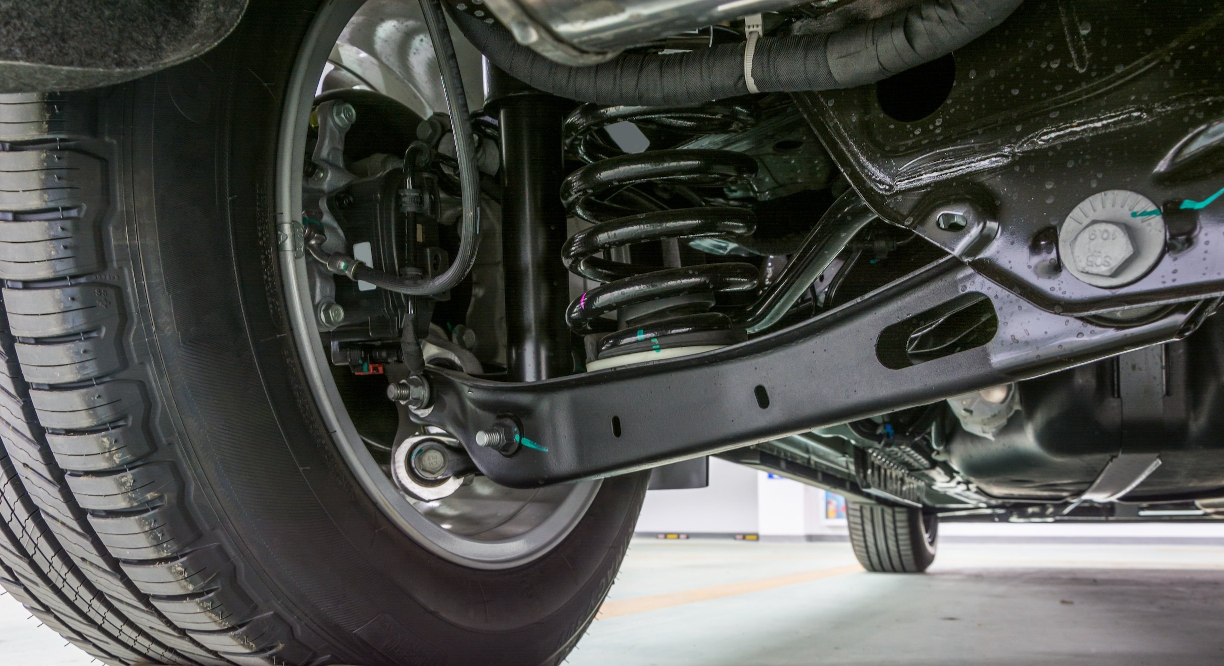 Close-up view of a vehicle's suspension system showing a coil spring, control arm, and wheel assembly.