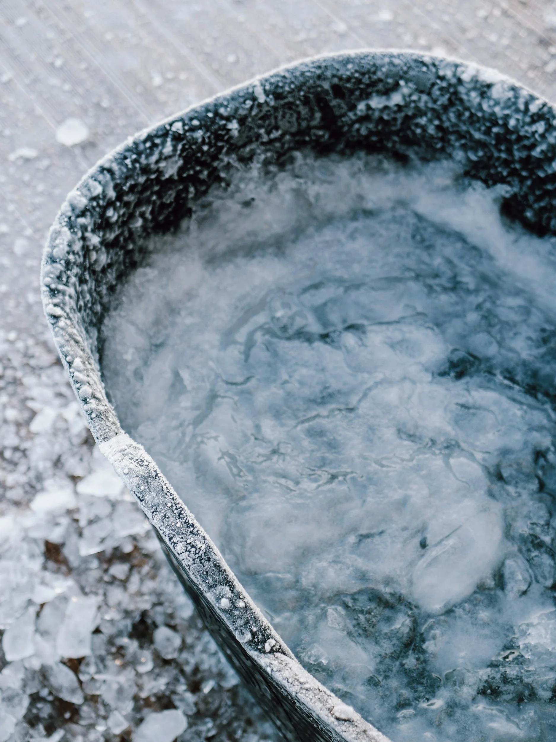 Ice in a black trash can on a surface covered with snow and ice.