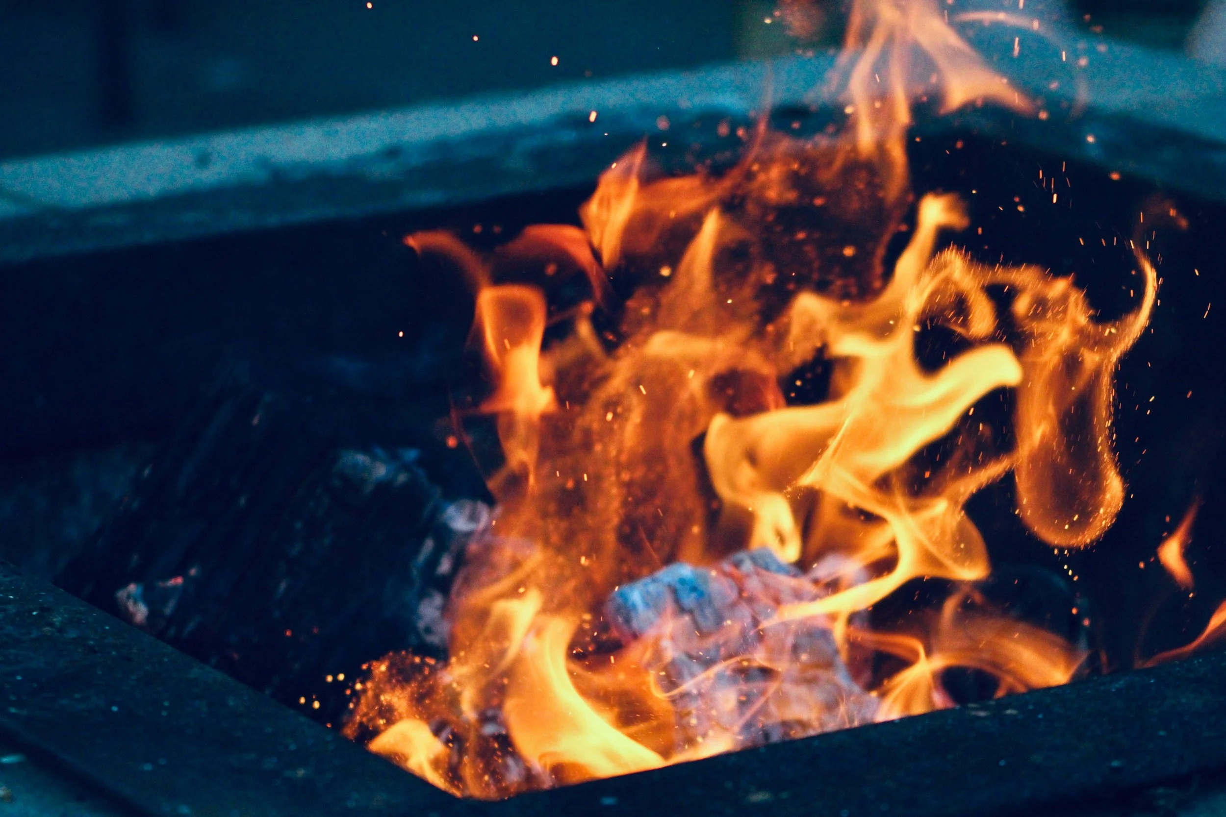 Close-up of a controlled fire in a metal fire pit with bright orange flames and glowing embers.