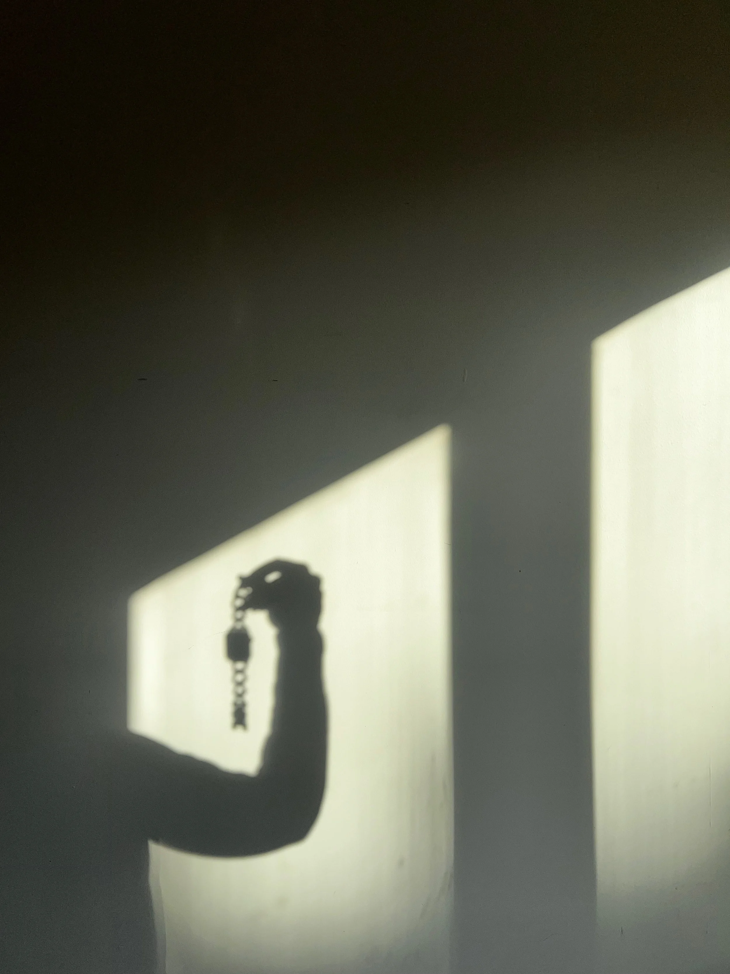Shadow of a person holding a keychain with keys on a wall, cast by sunlight through a window.