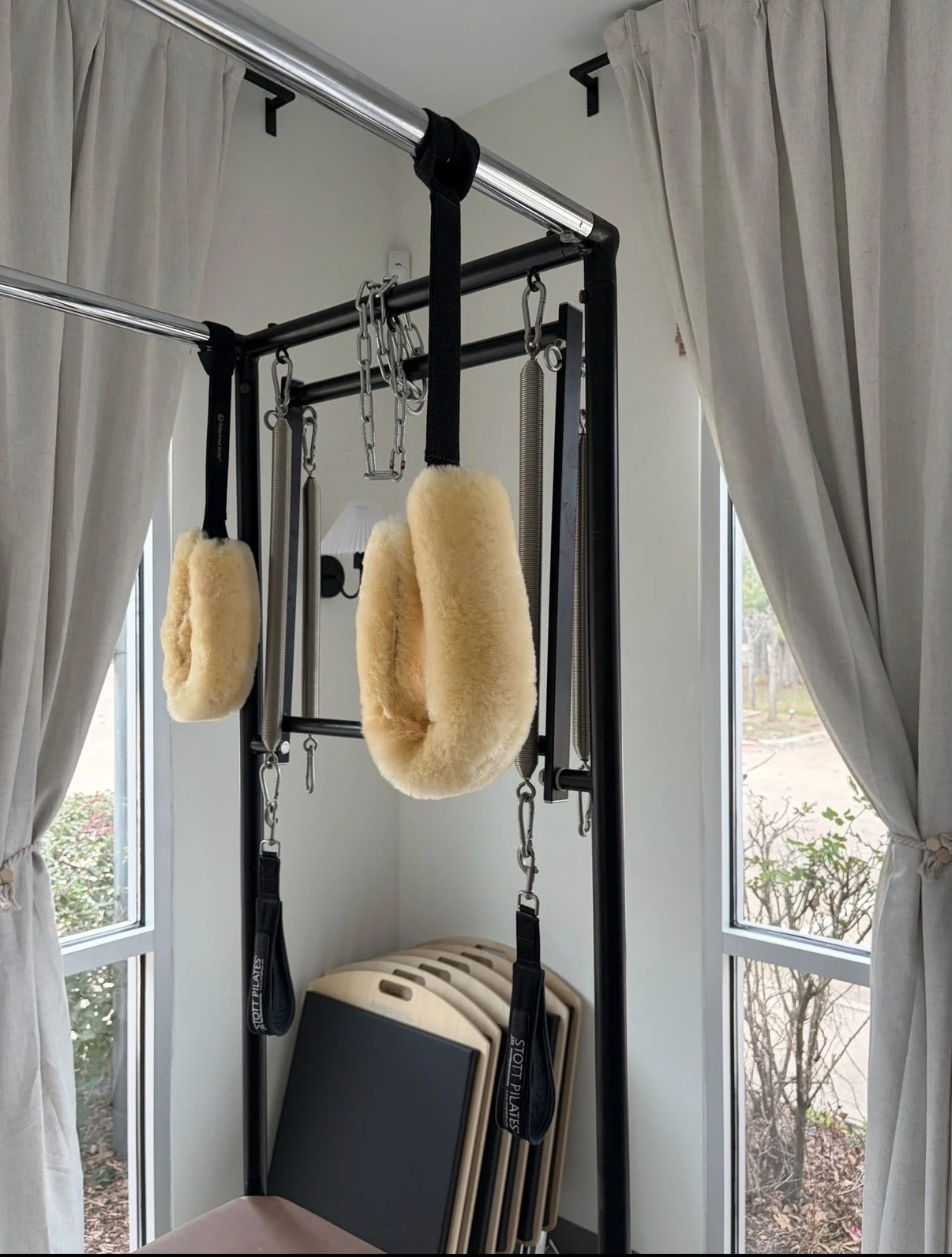A home gym setup with a pull-up bar, padded rings, resistance bands, and stacking aerobic steps near a window with curtains.