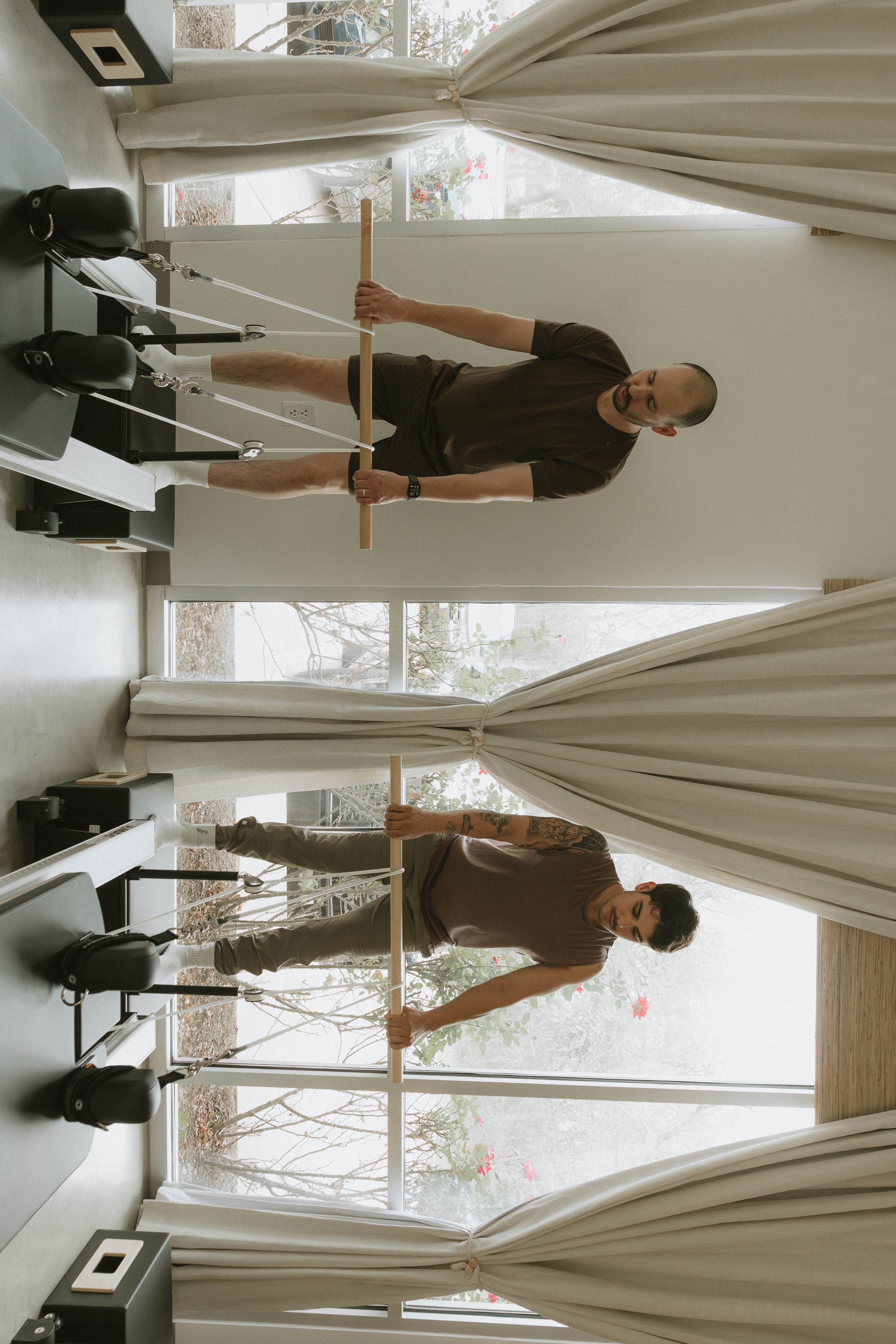 Two women exercising on Pilates reformers, demonstrating squats, in a fitness studio.
