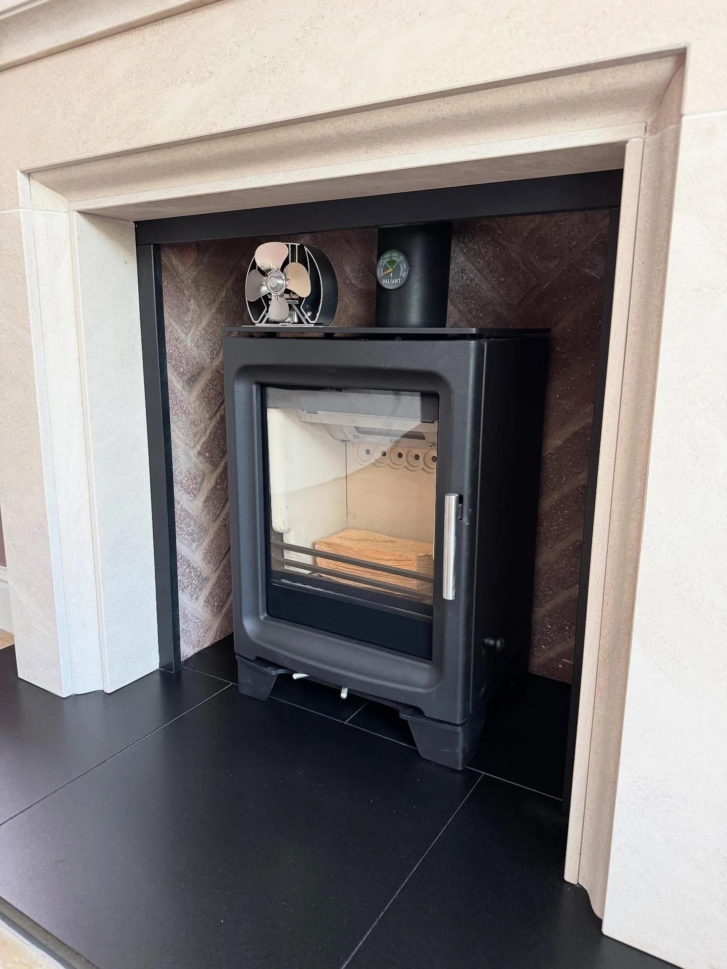 A stunning blend of texture and tone &mdash; granite hearth and limestone slips frame a Purevision stove set in a herringbone brick chamber. Finished with a premium stove fan and diffuser from The Stove Fan Company for warmth with style. All products