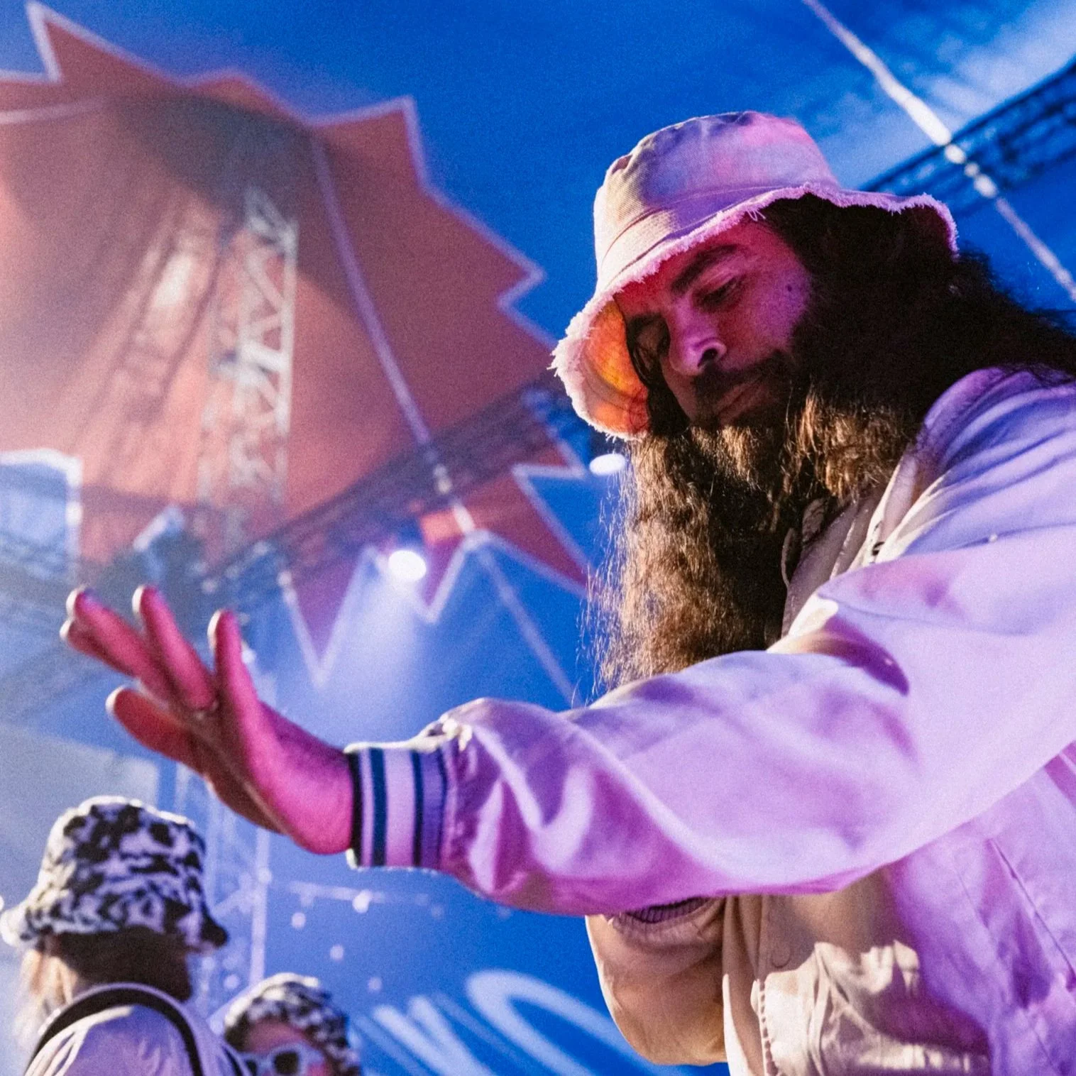 Simon Lingmerth wearing a bucket hat, dancing and performing at an event with vibrant stage lighting and a large red star sign in the background.
