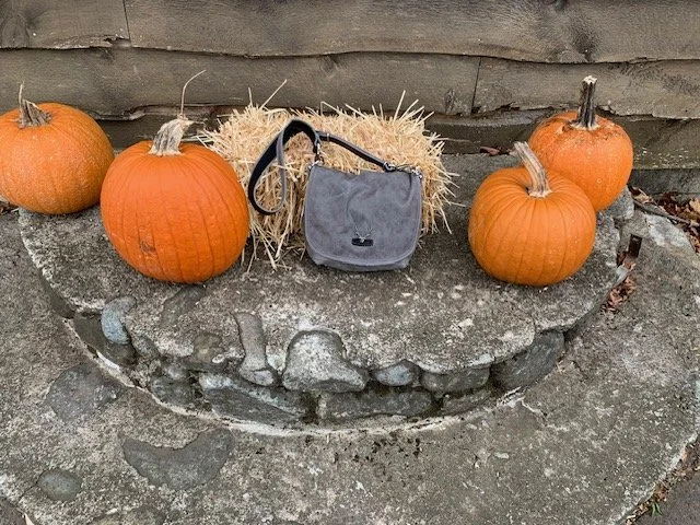 Four pumpkins on a stone ledge with a Eustis Stag purse and straw in the center; ATCo. is the brand that offers functional and stylish leather handbags built to last.
