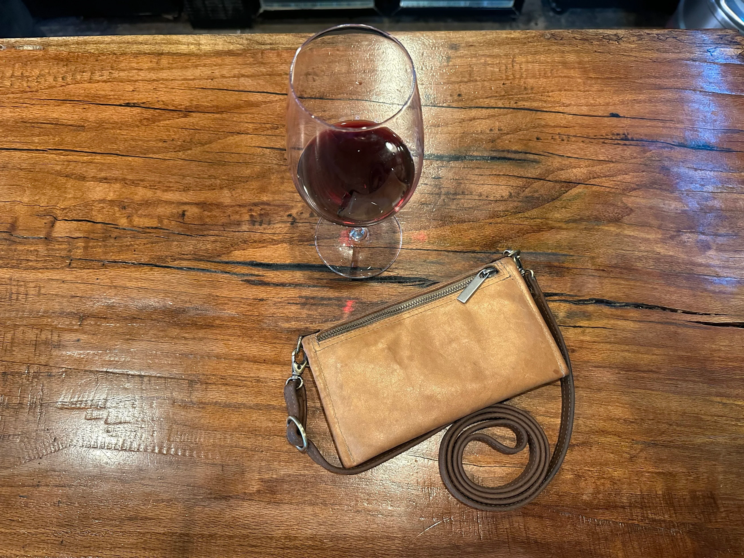 A glass of red wine on a wooden table with a Castine.