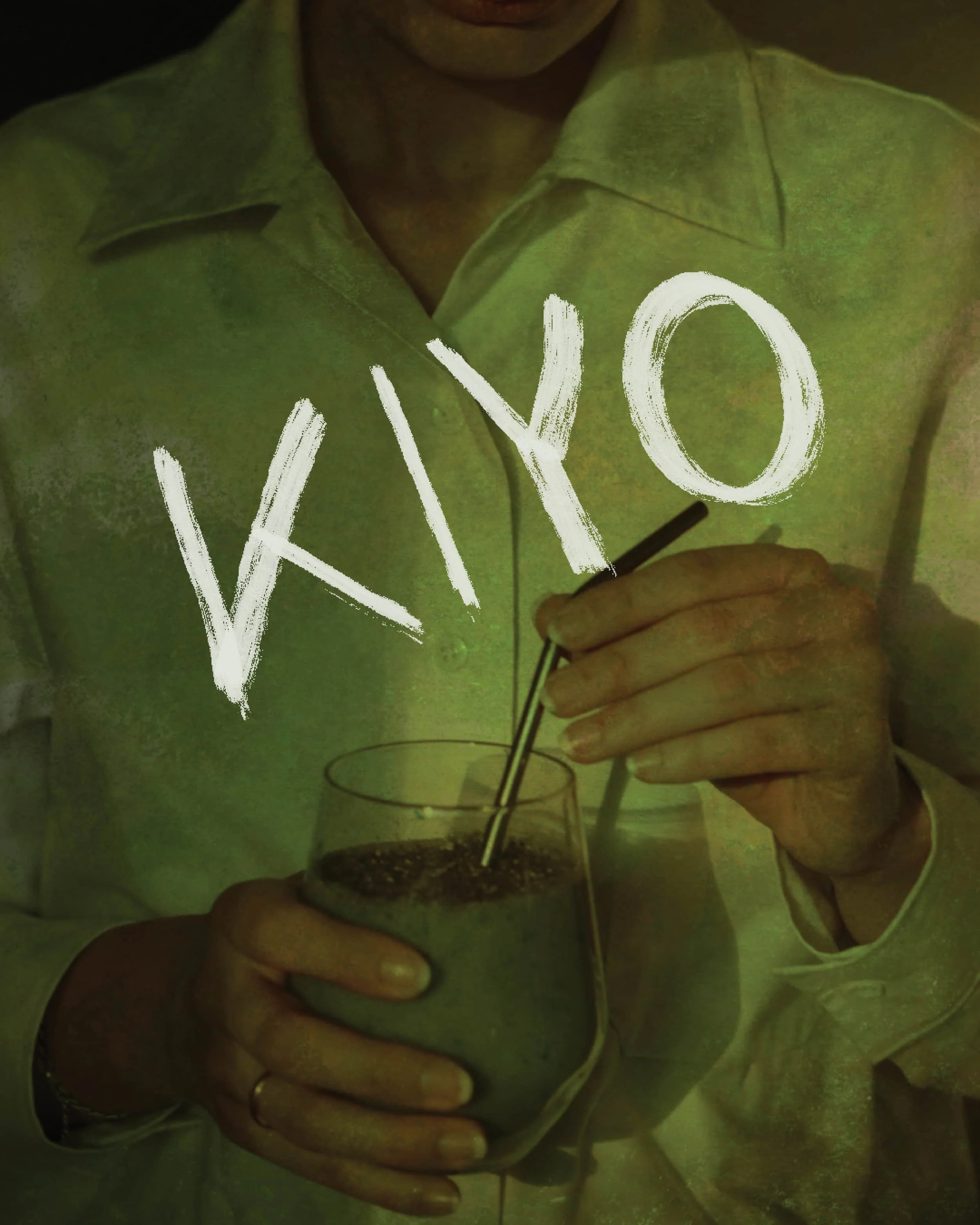 A woman in a light-colored shirt holding a glass of green smoothie and stirring it with a black straw. The word 'VYO' is written across the image in white, brushstroke-style letters.