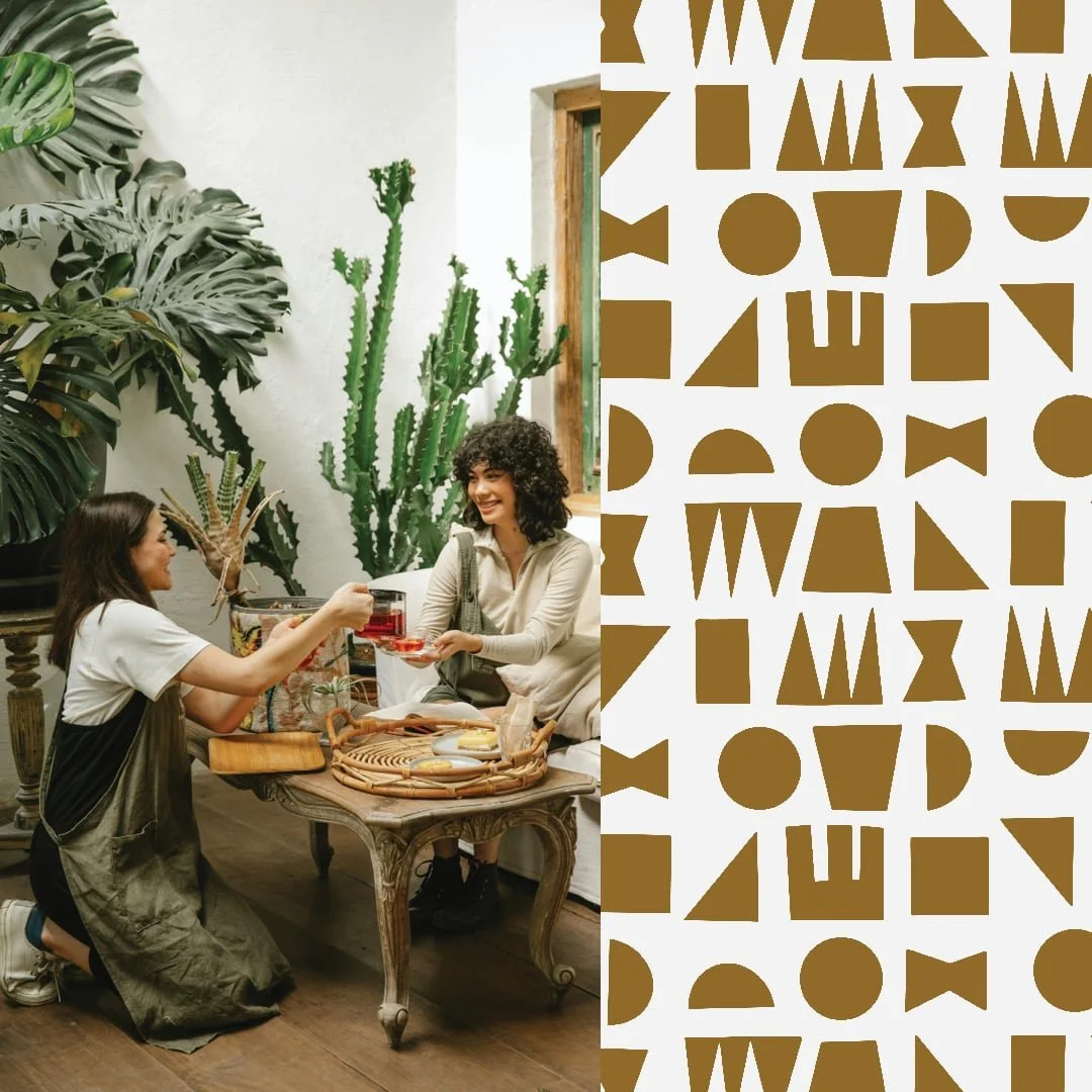 Two women are having a tea or coffee toast in a cozy indoor setting with large green plants, including a tall cactus and a monstera, beside a wooden window.
