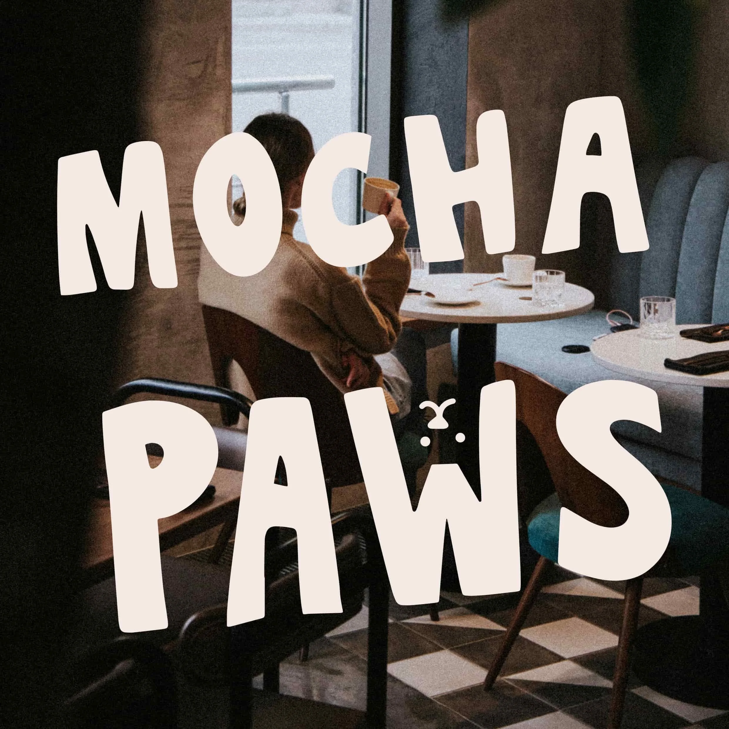 A person sitting at a restaurant table drinking coffee or tea, with a sign spelling 'MOCHA PAWS' overlaid on the image.