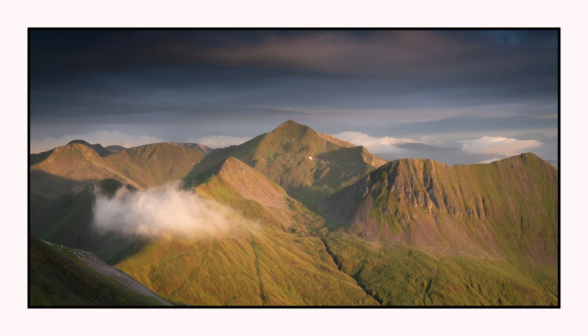 Sunlit green mountains with clouds in the sky, viewed from a scenic vantage point.