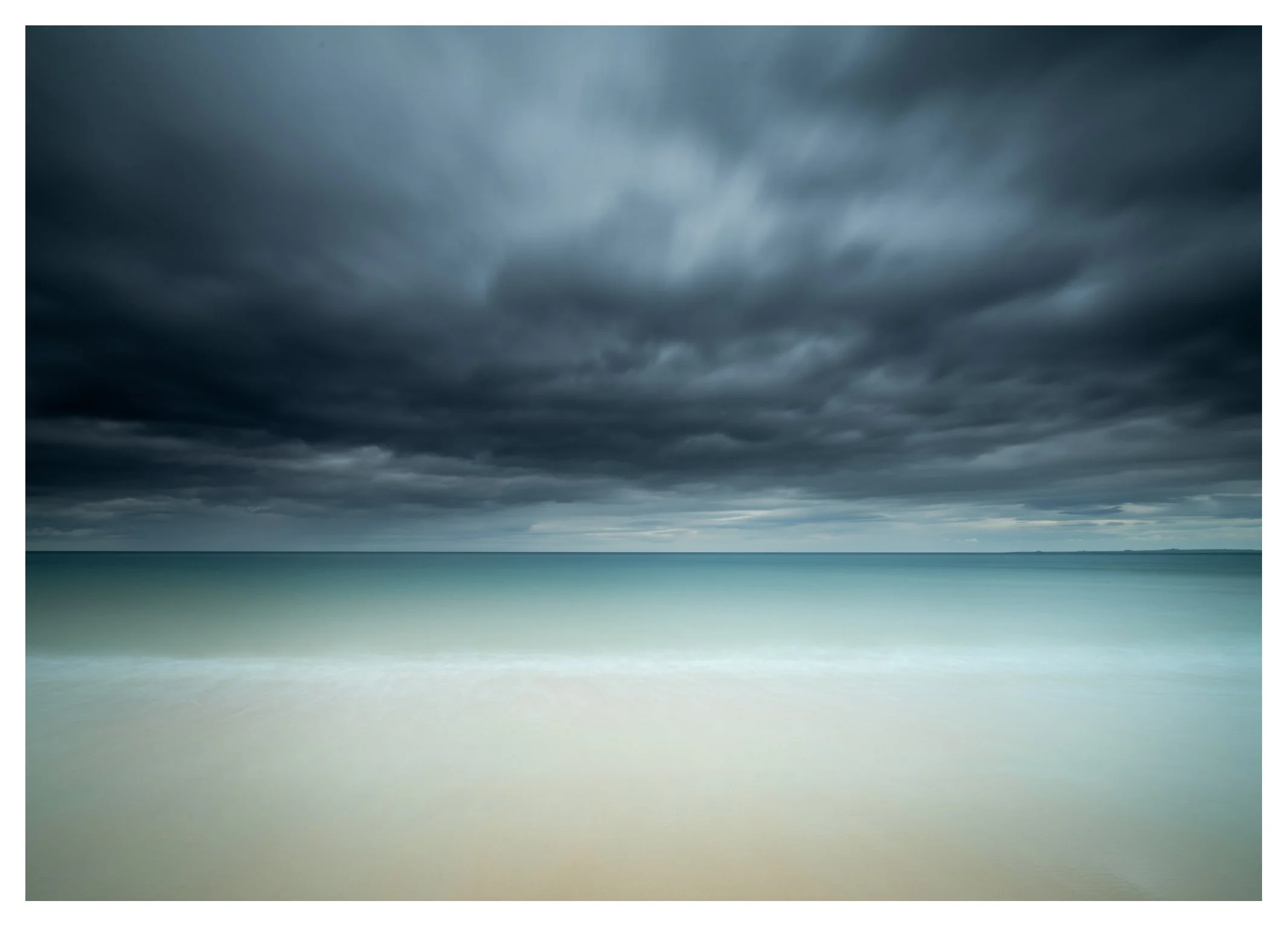 Dark storm clouds over a tranquil ocean with sandy beach in the foreground.