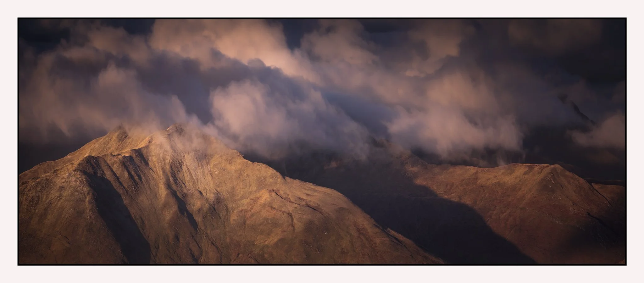 A mountainous landscape with rugged hills and peaks under a cloudy sky at dusk or dawn.