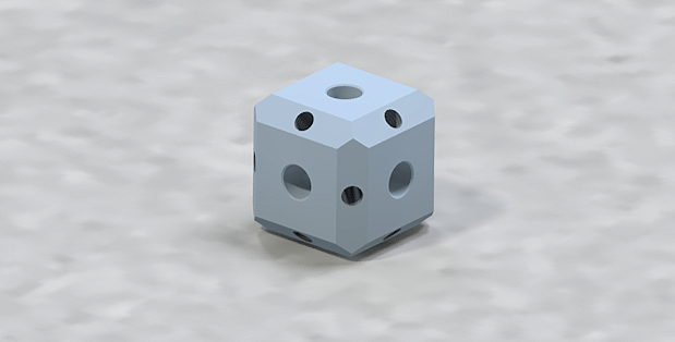 A gray, six-sided die with circular holes on each face, placed on a textured gray surface.