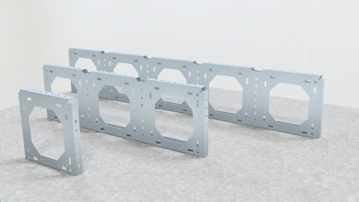 Multiple silver metal framing panels with large central cutouts and various holes, arranged in a group on a light gray textured surface against a plain white background.