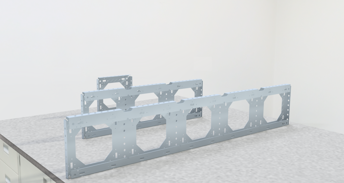 Three steel single plate element structures with hexagonal cutouts placed on a gray speckled countertop in a room with plain white walls.