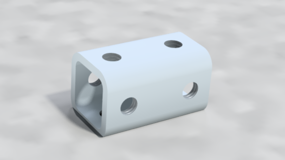 A white metal block with four circular holes, two on the top surface and two on the side, sitting on a gray surface.