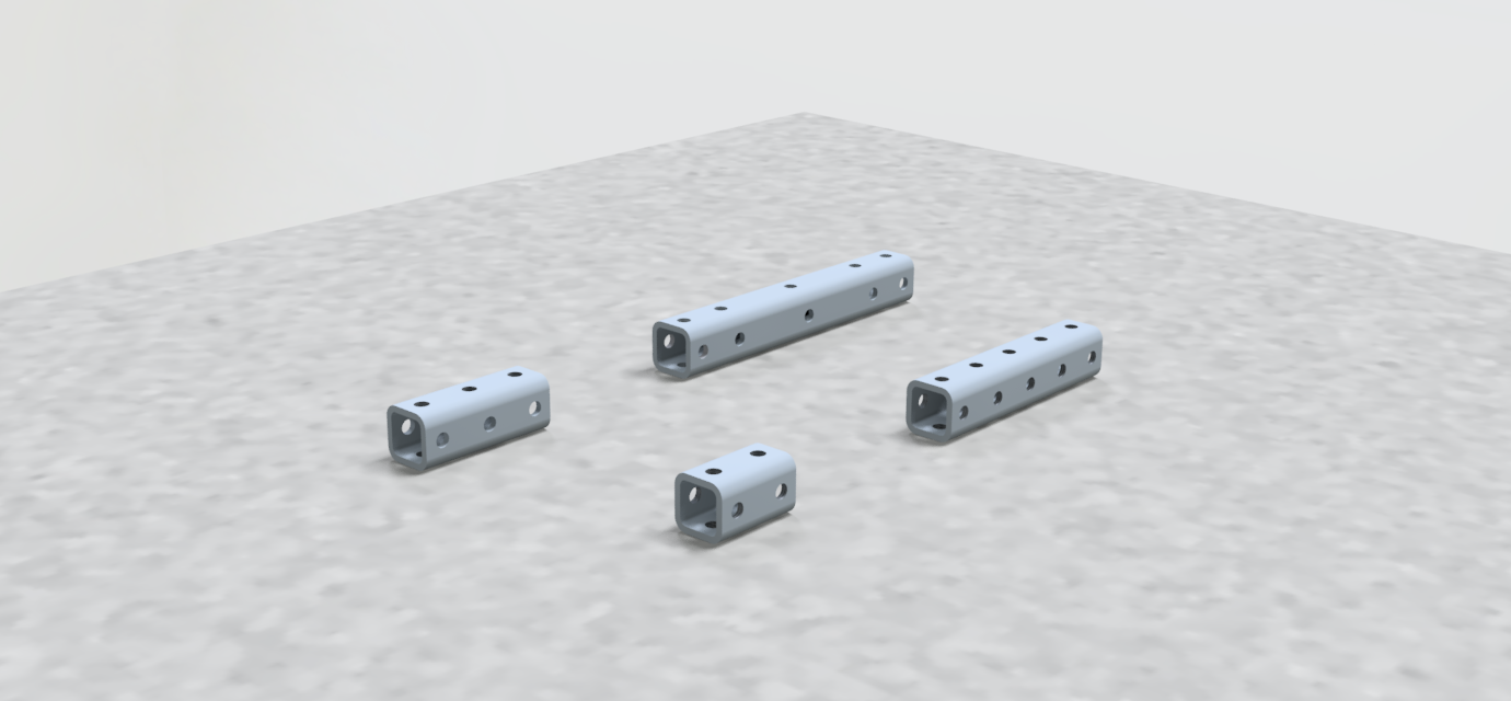 Four gray metal rectangular blocks with multiple holes are arranged on a light gray speckled surface.