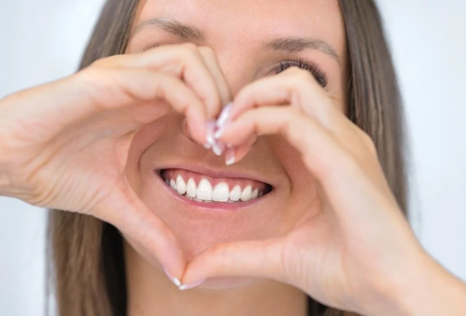 Woman smiling and making a heart shape with her hands against a background resembling water.