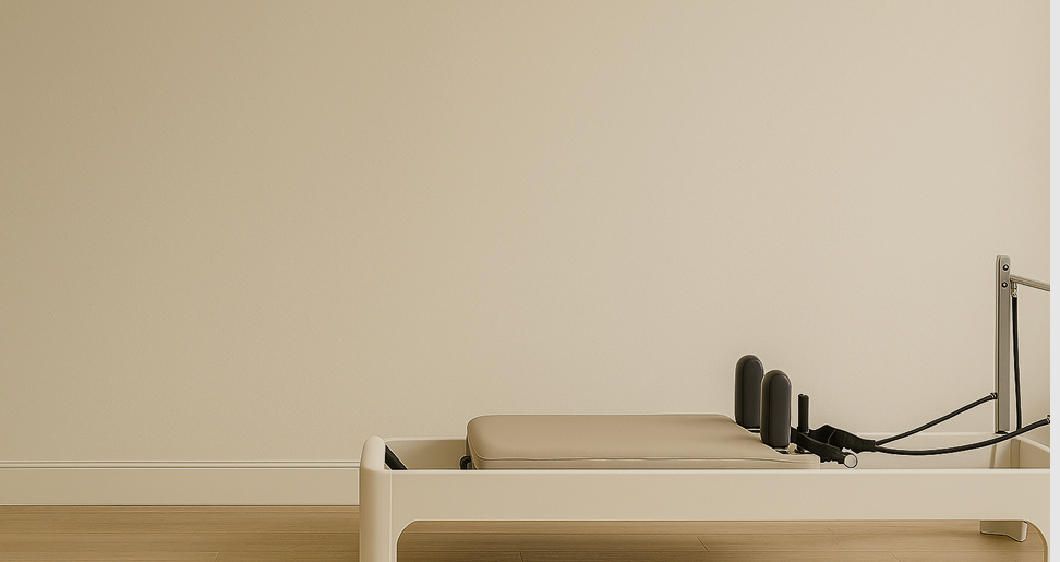 A minimalist physical therapy or Pilates reformer machine with padded platform and resistance bands against a plain wall.