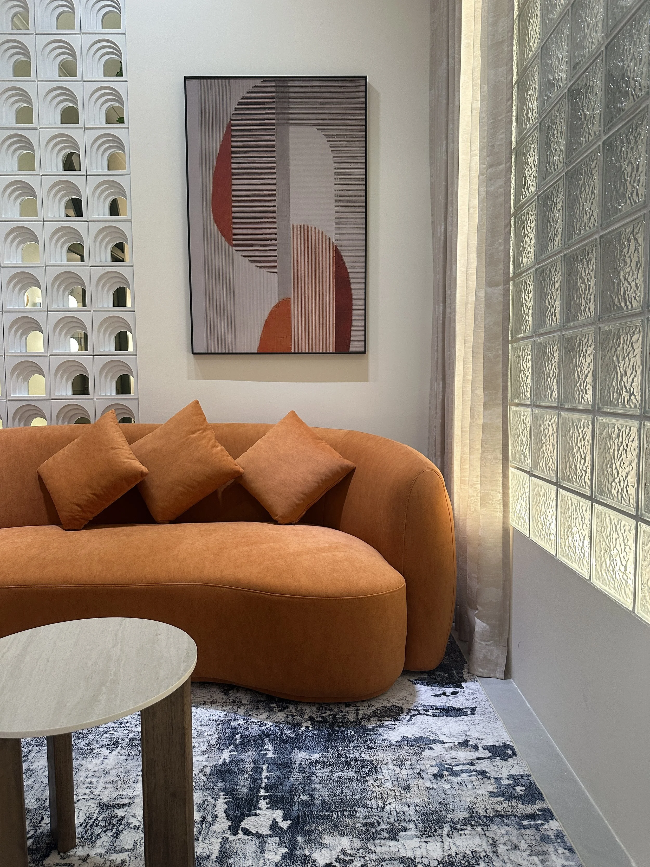 Curved orange sofa with soft textured fabric and matching toss pillows for a cozy finish. Beside glass blocks and arched feature wall
