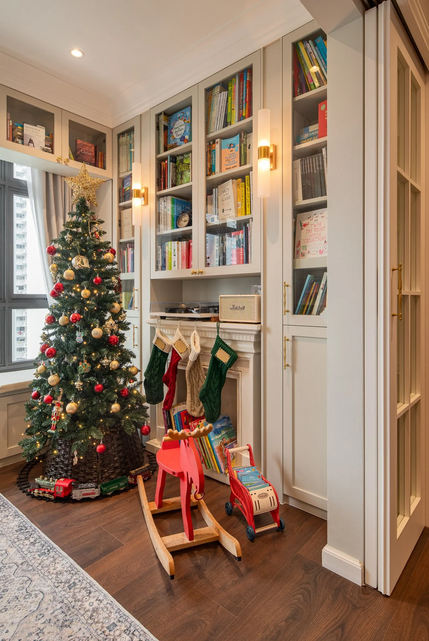 Library with white built-in bookshelves, Christmas tree,  brass wall lights and fireplace