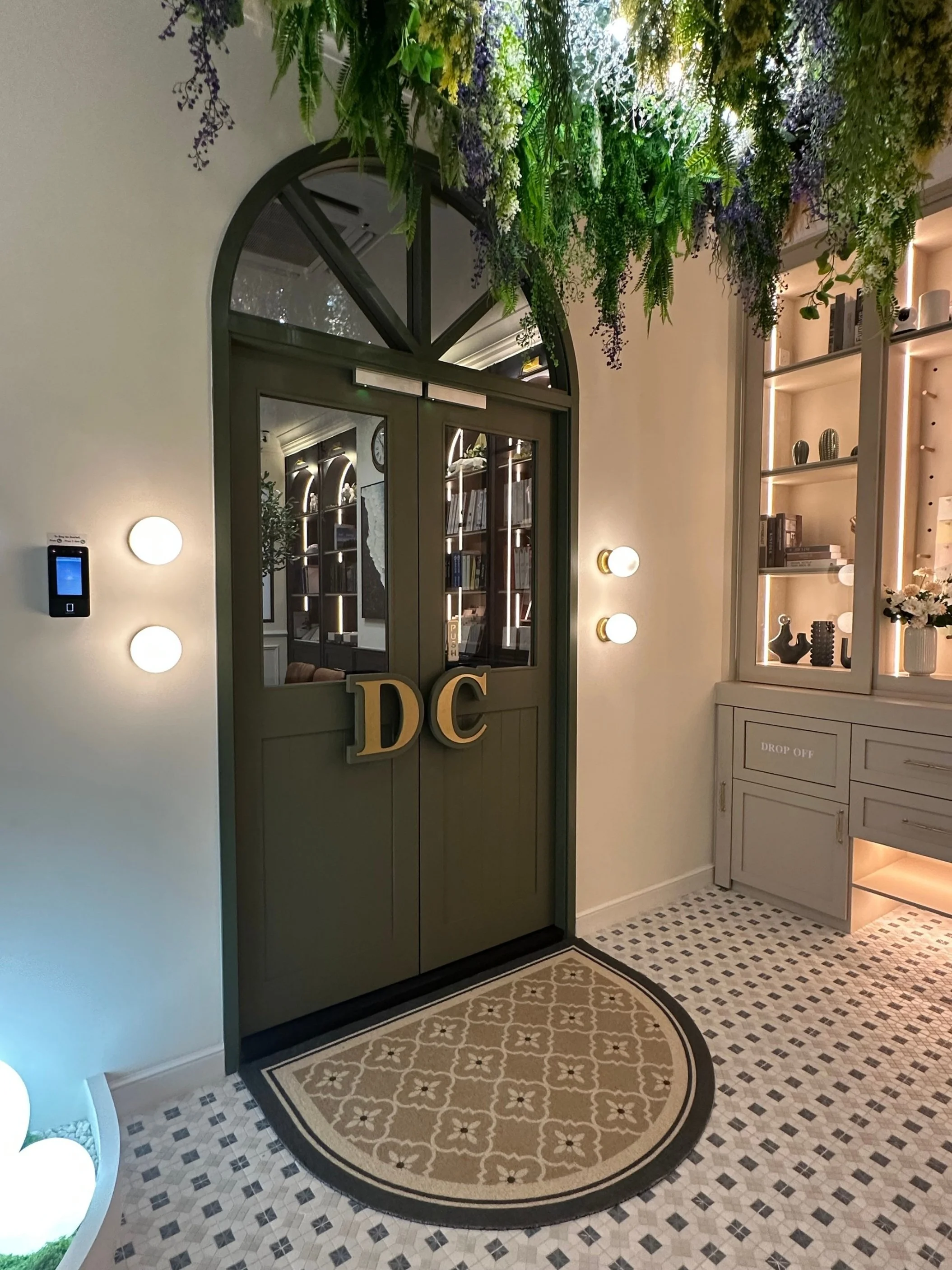 DeCurio Studio foyer with arched french doors in sage, gold brass signage, patterned tiles and hanging greenery