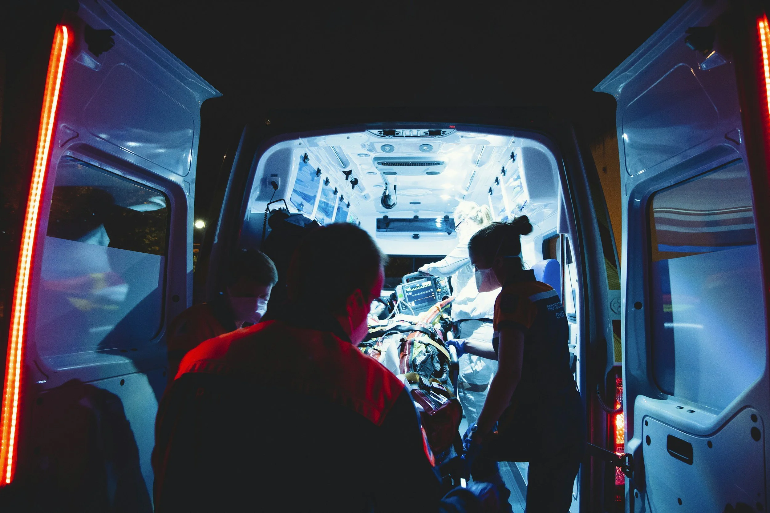 Emergency medical team in an ambulance attending to a patient during night time with interior blue lighting.