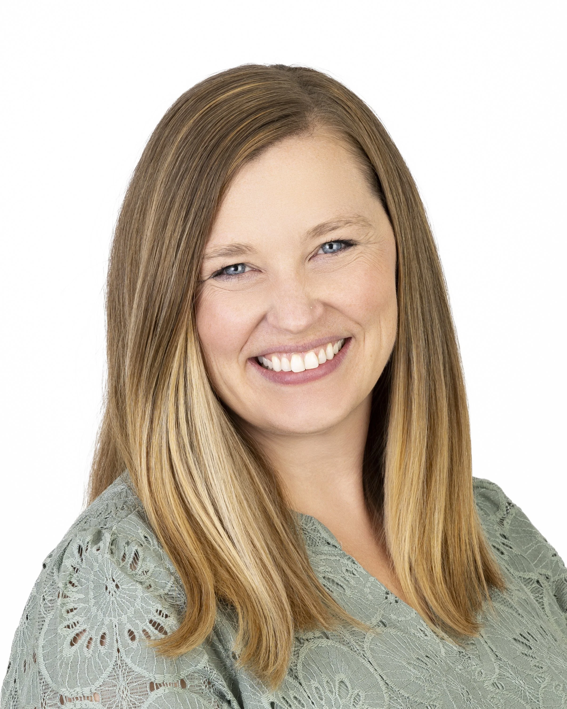 Close-up of a smiling woman with long, straight, light brown hair, wearing a light green lace top, against a white background.