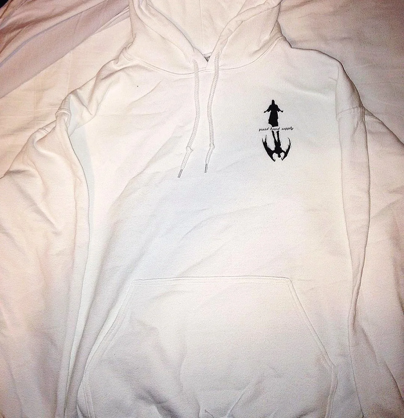 White hoodie with a small black graphic of a figure with open arms and a reflection below it, located on the left chest area.