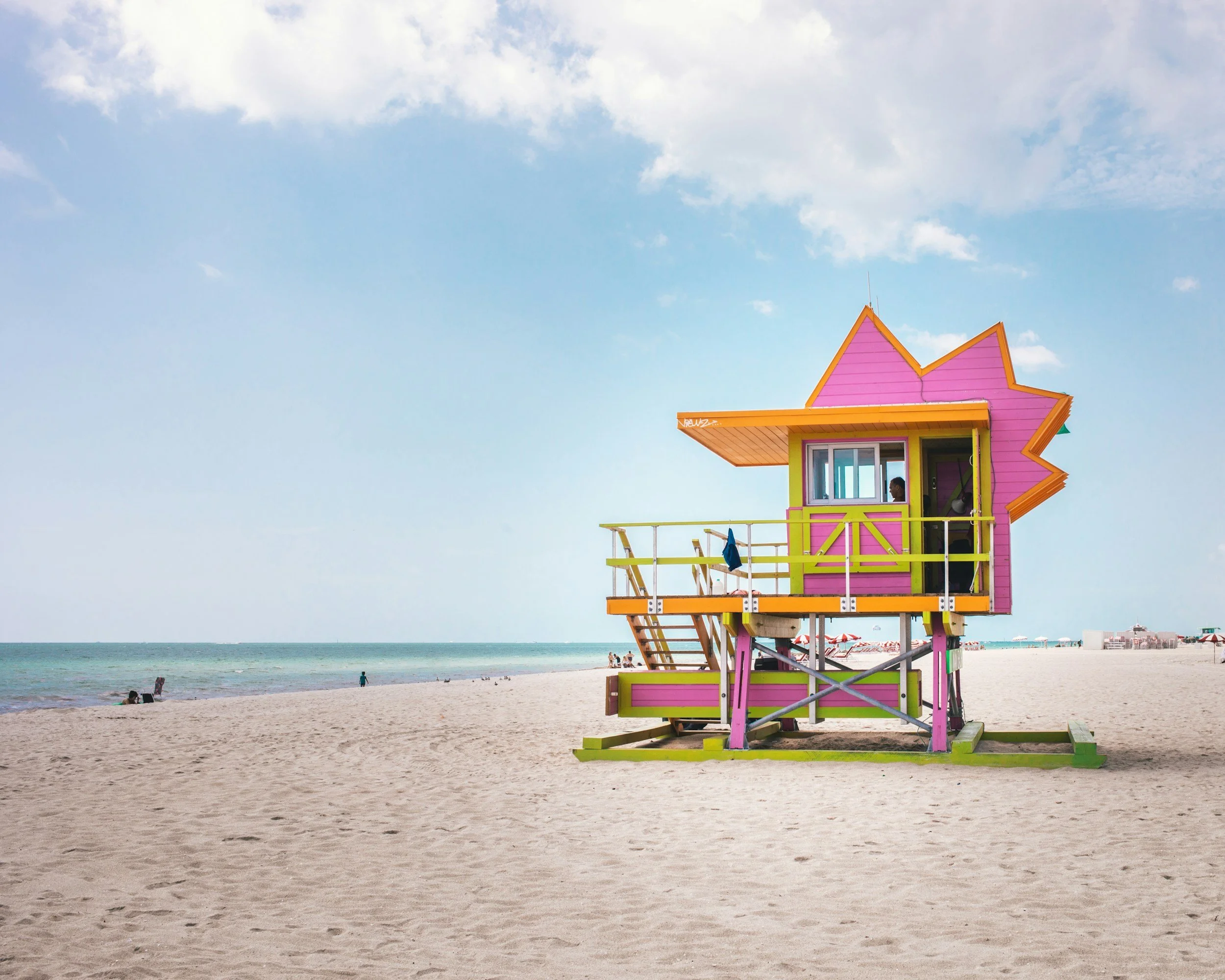Colorful lifeguard tower on a sandy beach with the ocean and sky in the background.