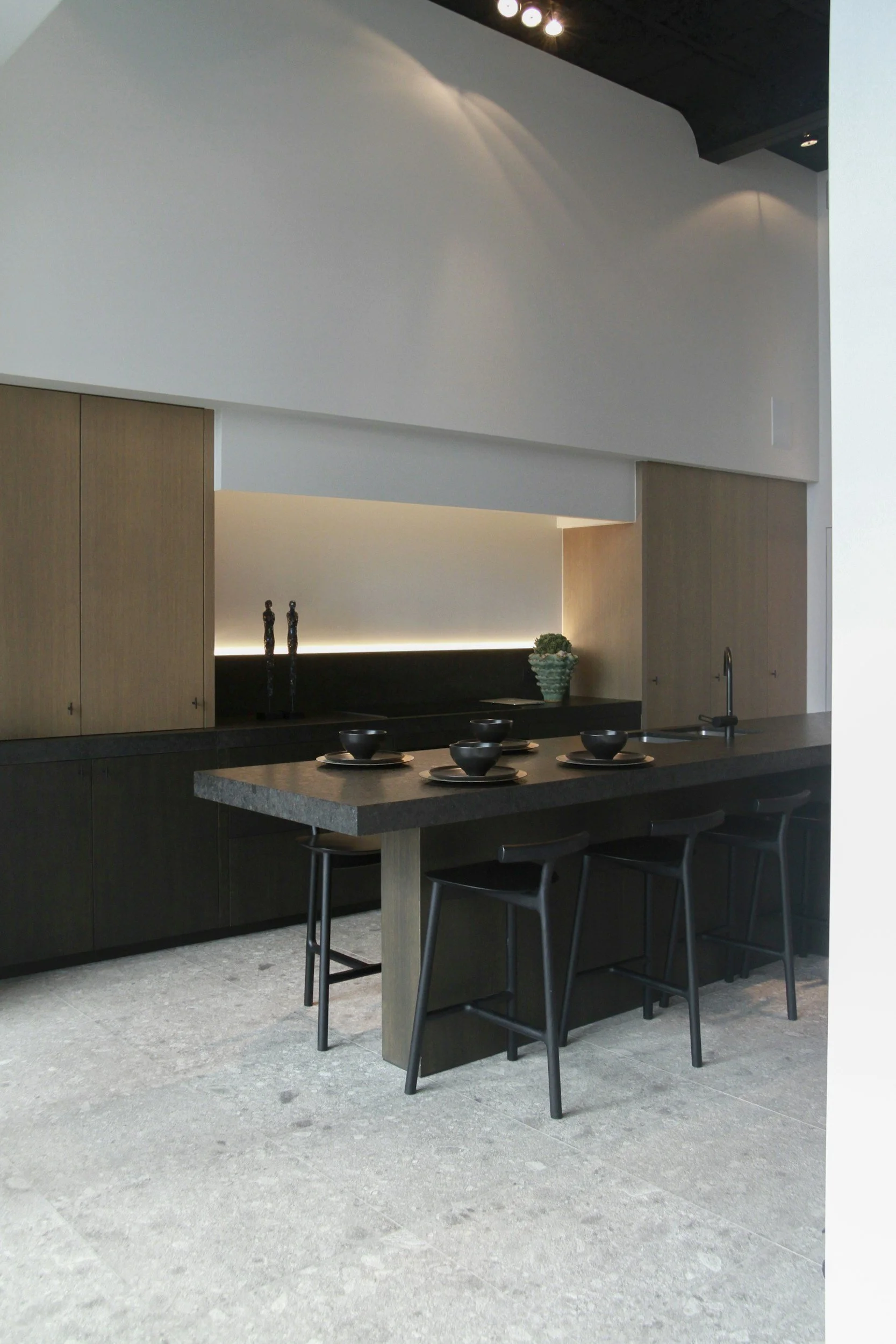 Modern kitchen with black and wooden cabinets, a dark countertop, and a dining area with four black chairs and black bowls and plates