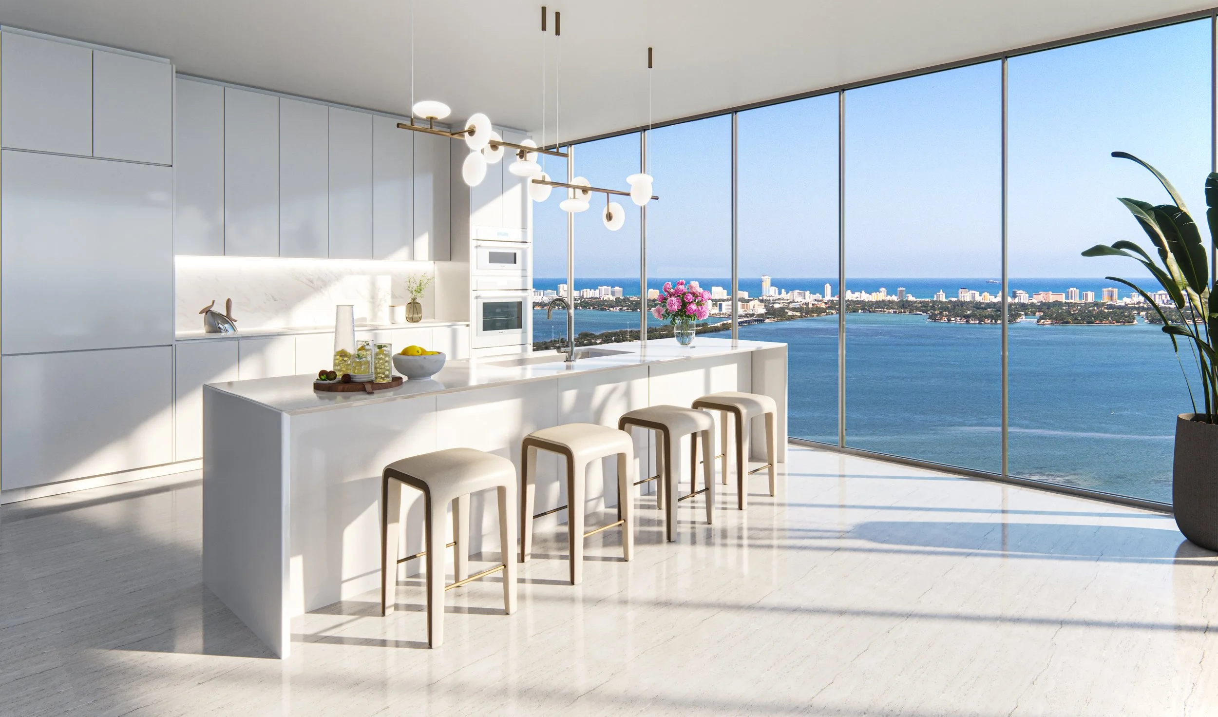 Modern kitchen with white cabinets and island, bar stools, large windows with a view of a city and water, pink flowers in a vase, and decorative items on the counter.